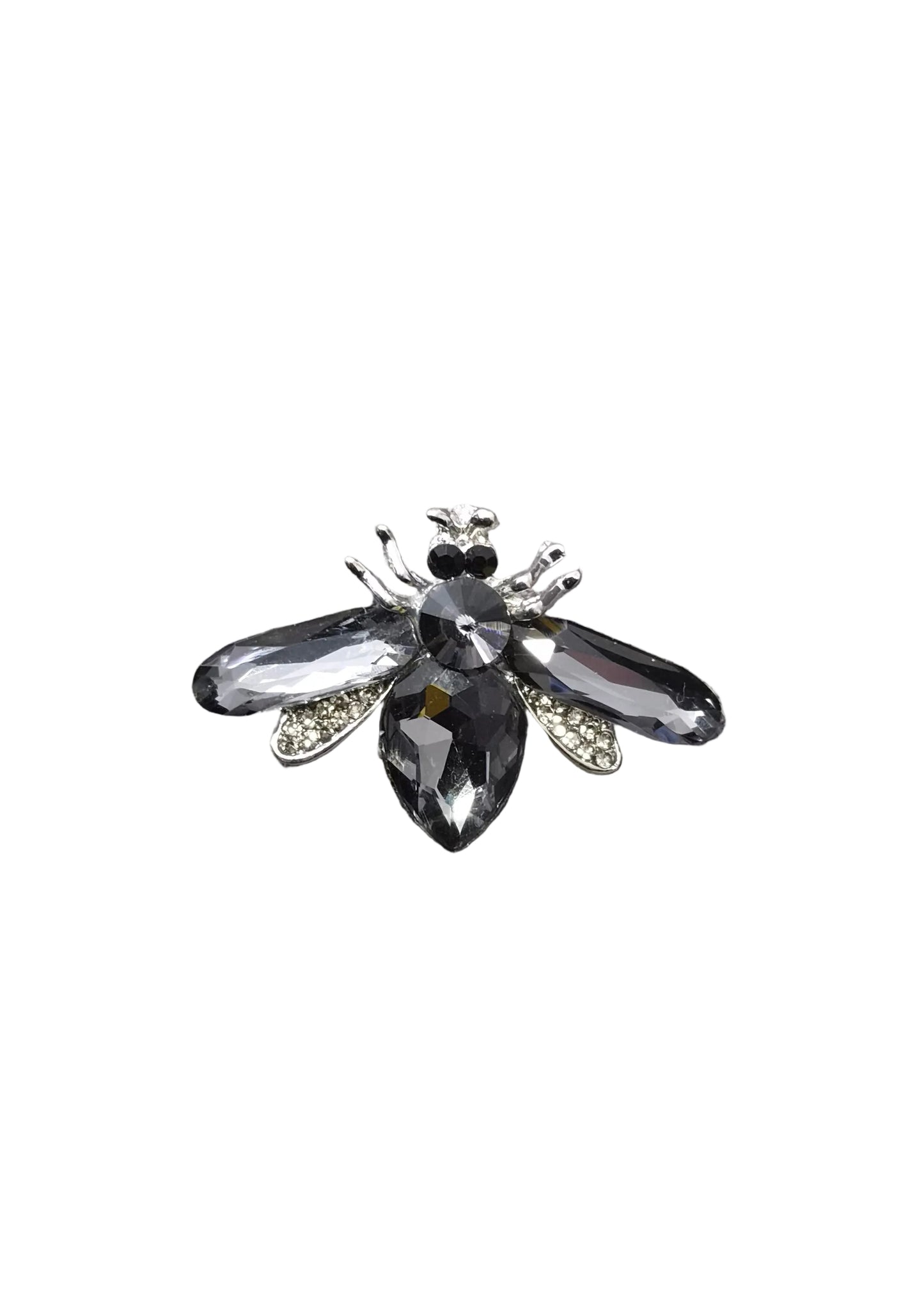 A black crystal bumblebee brooch with silver-toned metal details, displayed on a textured gray fabric surface with a yellow ruler at the bottom for scale.