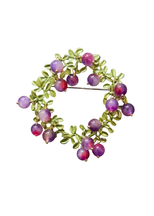 A gold-toned brooch featuring green leaf motifs and small round purple beads.