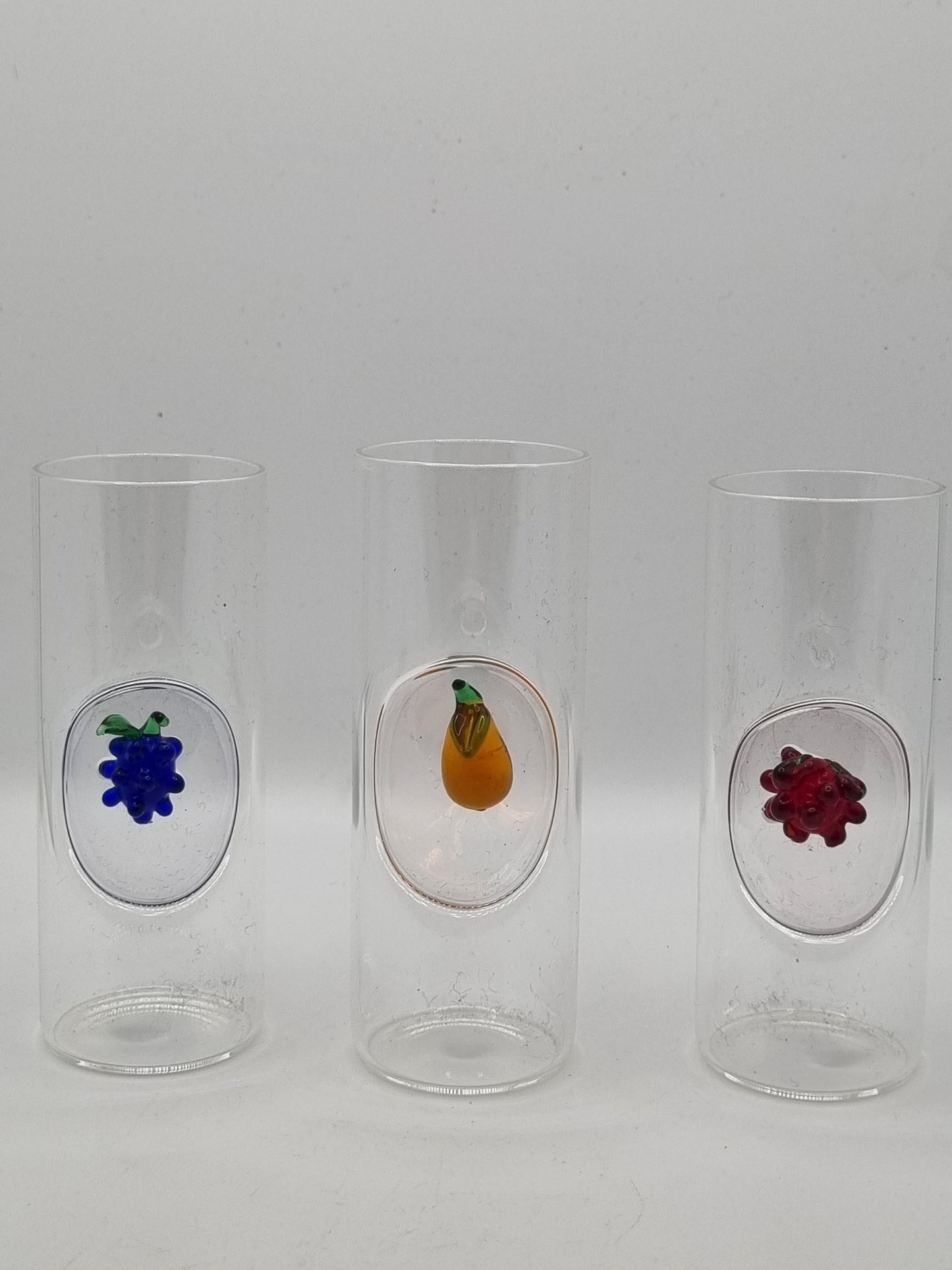 Three small round shot glass with colourful fruit insets - blue grapes, red grapes and yellow pears