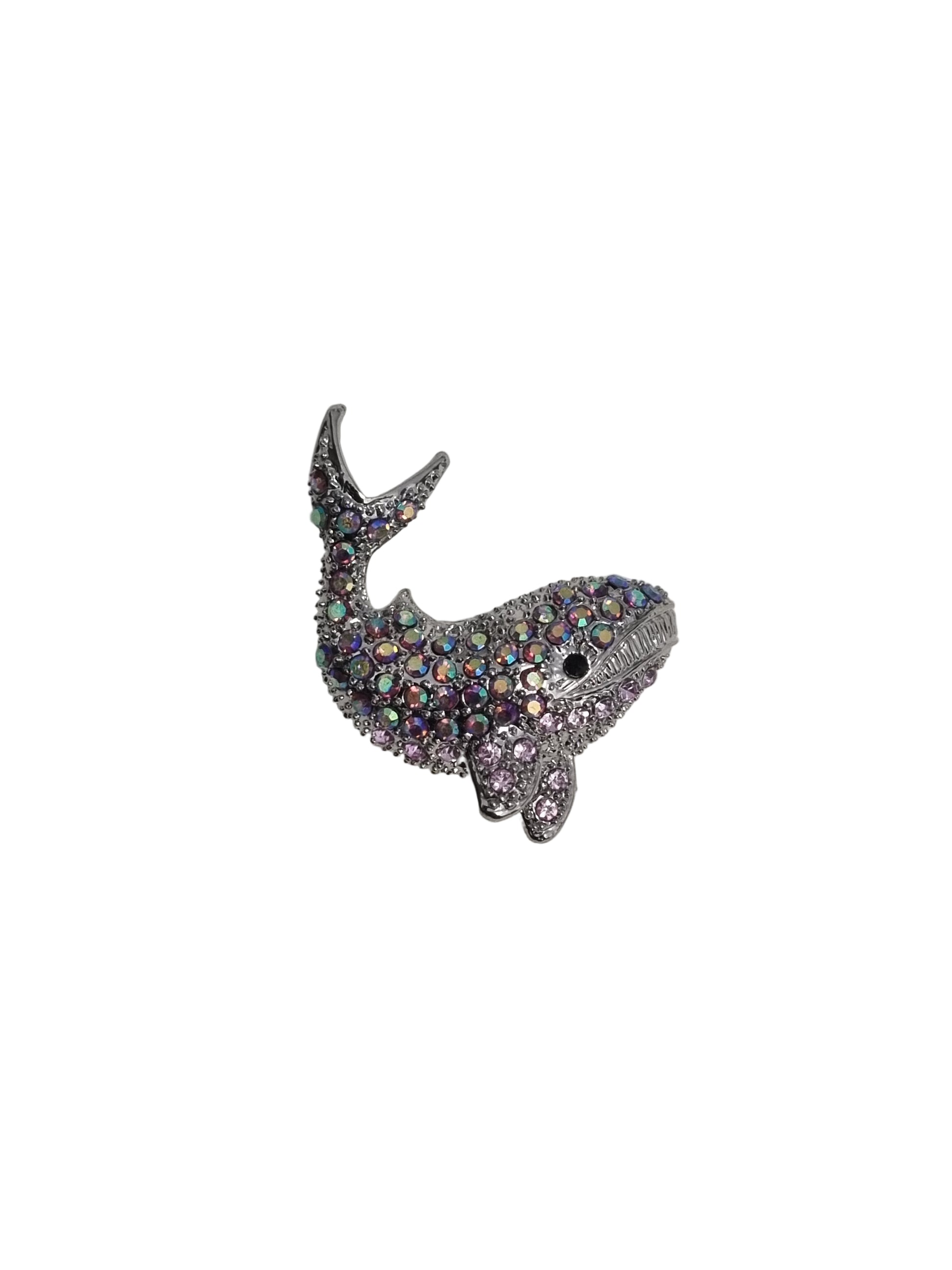 Shiny whale-shaped brooch on a white fabric background