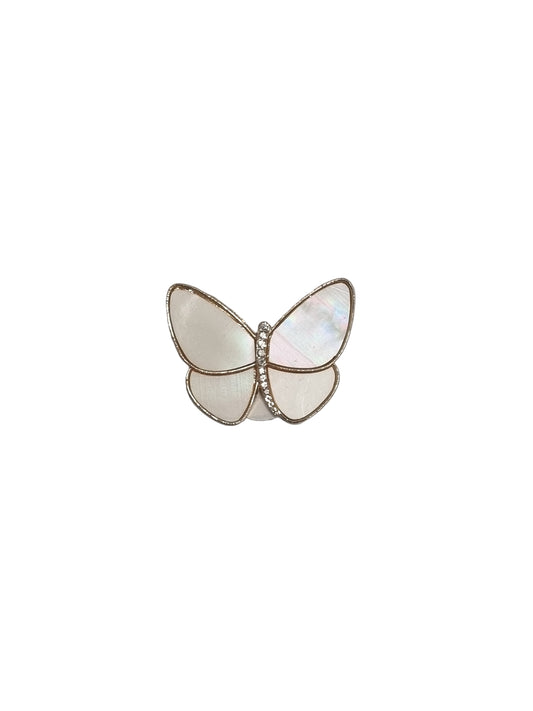 Butterfly-shaped brooch with white and gold details on a gray fabric background
