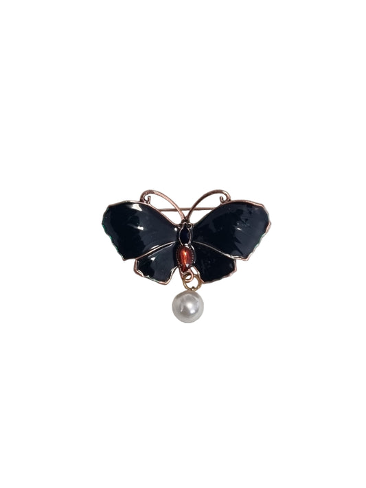 Butterfly-shaped brooch with black stones, red gem, and pearl on a light gray background
