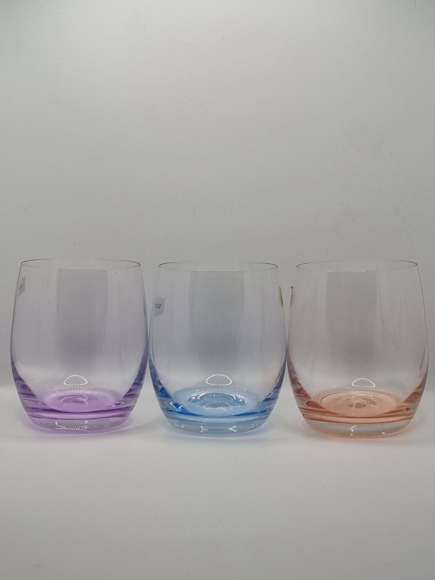 Set of three whiskey tumblers with red, purple and blue bases on a light grey background