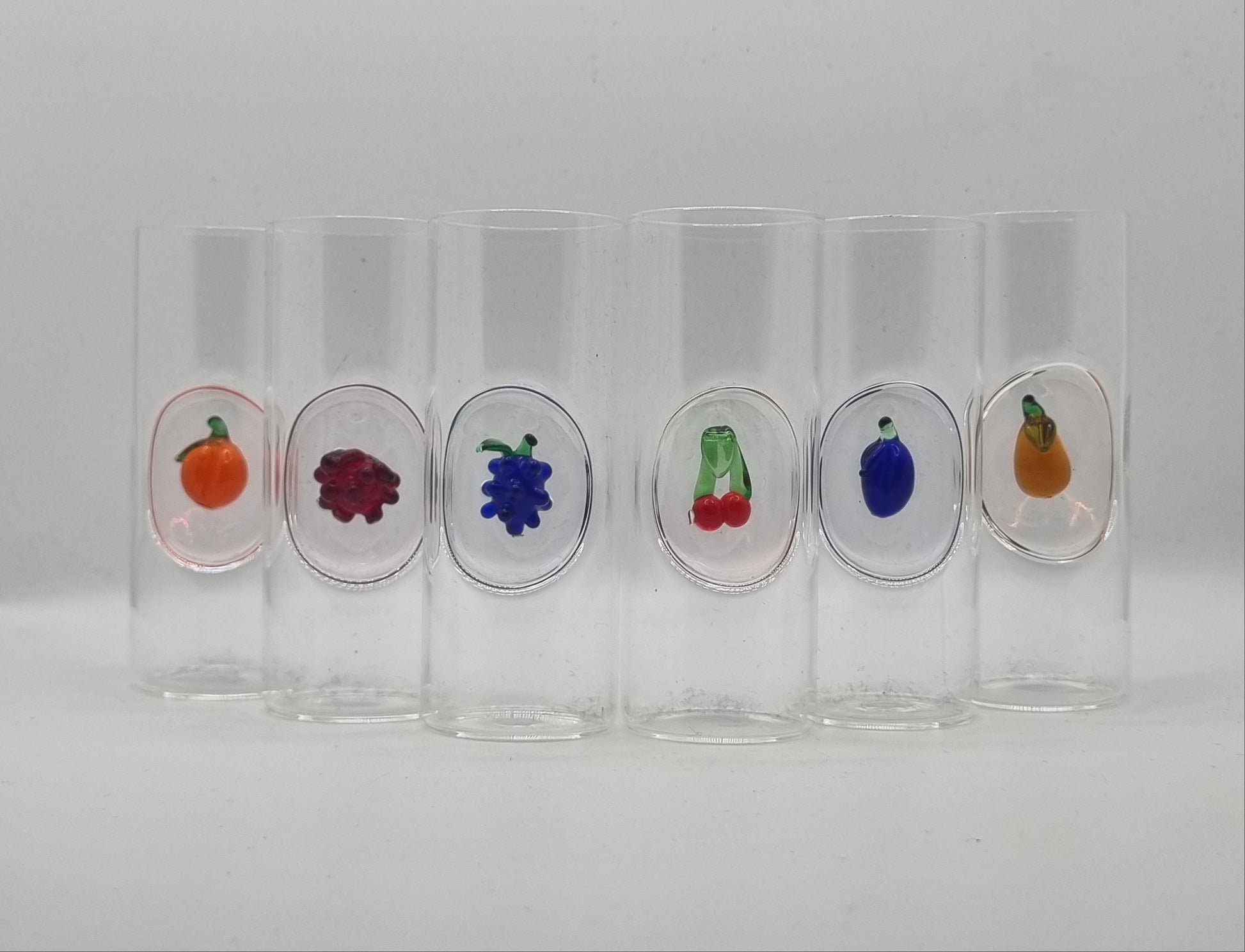 Set of clear glass shot glasses with glass fruit designs on a white background