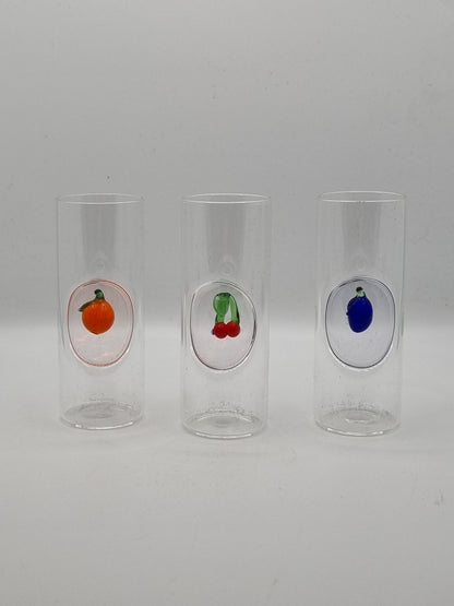 Three small round shot glass with colourful fruit insets - blue plum, red cherries and an orange