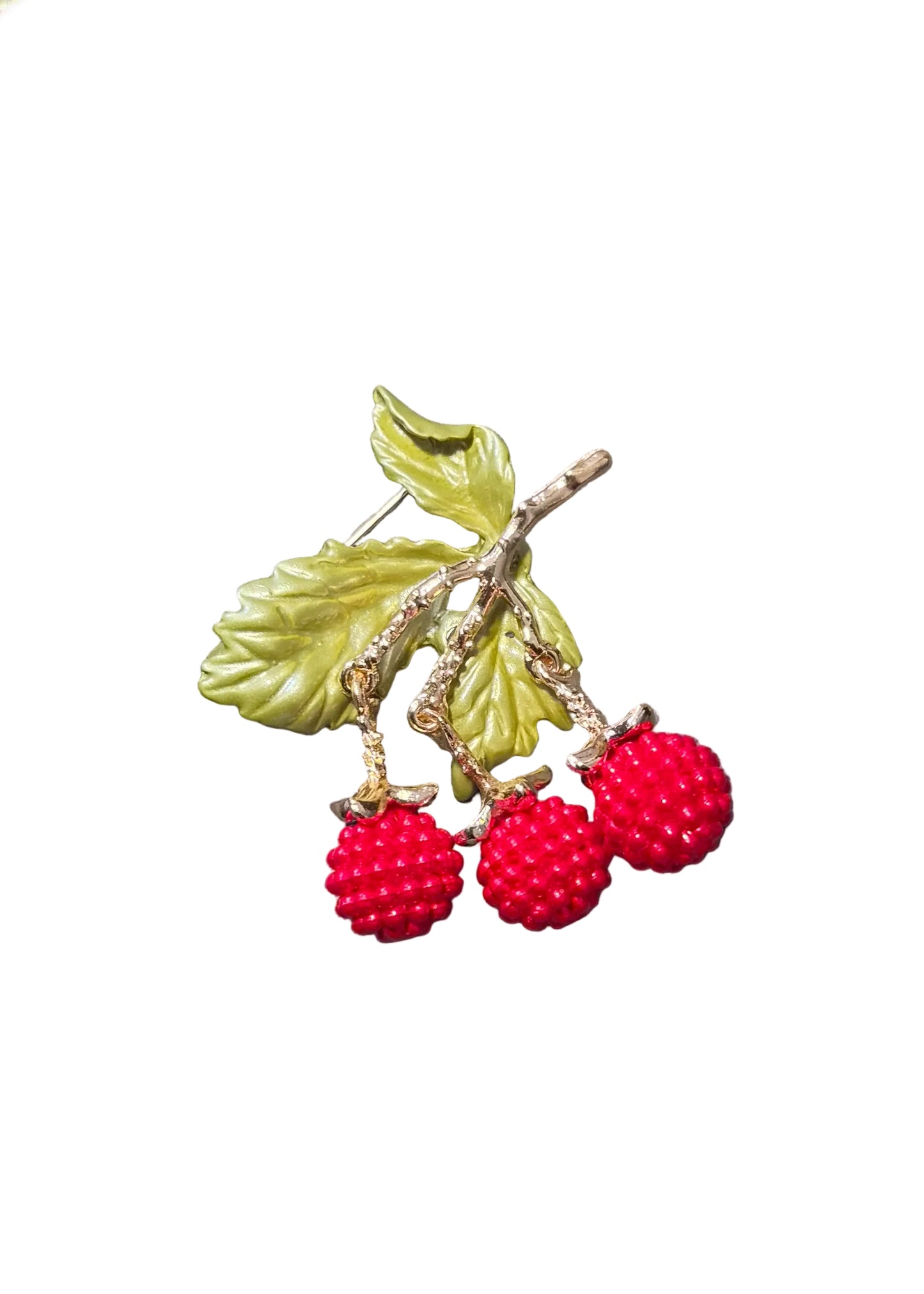 A close-up of a jewelry piece featuring three red raspberry-like beads on a gold branch with green leaves.